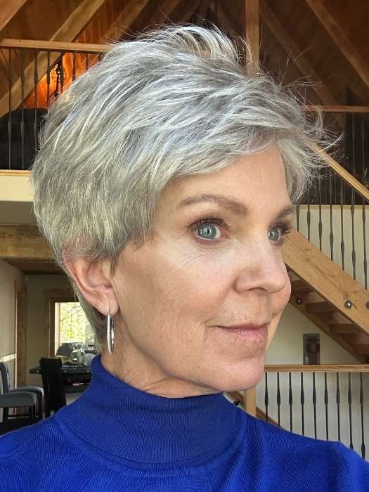 Mature woman wearing short silver pixie Ellen Wille Tab wig with natural hairline blue turtleneck and hoop earring
