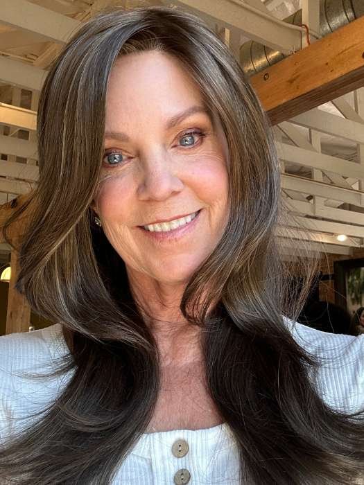 Smiling mature woman modeling Zara wig by Rene of Paris long layered brown hair with natural center part