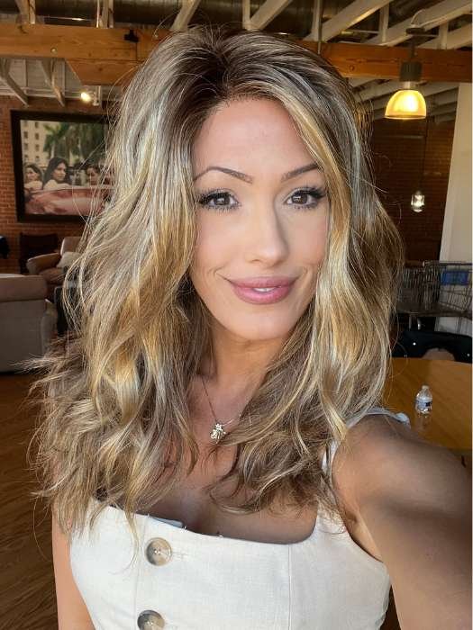 Smiling model wearing Ellen Wille Arrow lace front wig in warm blonde balayage with loose waves in loft setting