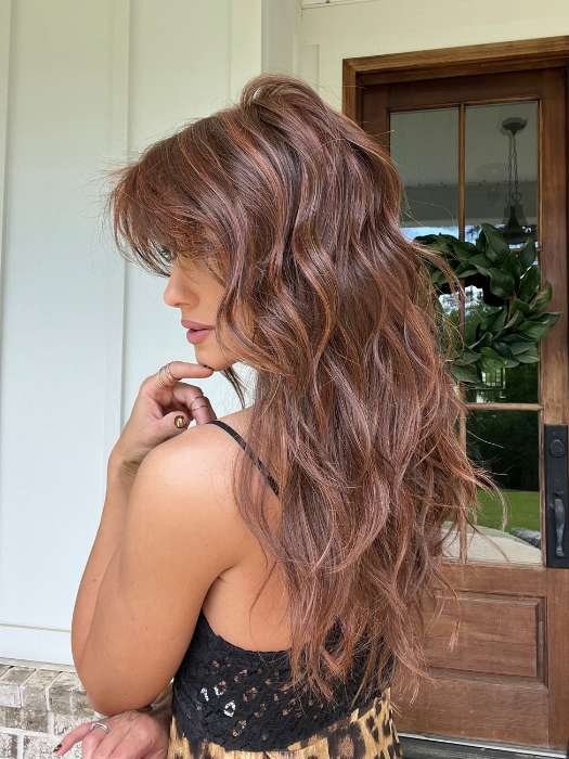 Side profile model wearing long wavy brown wig for women with layered bangs and natural loose waves